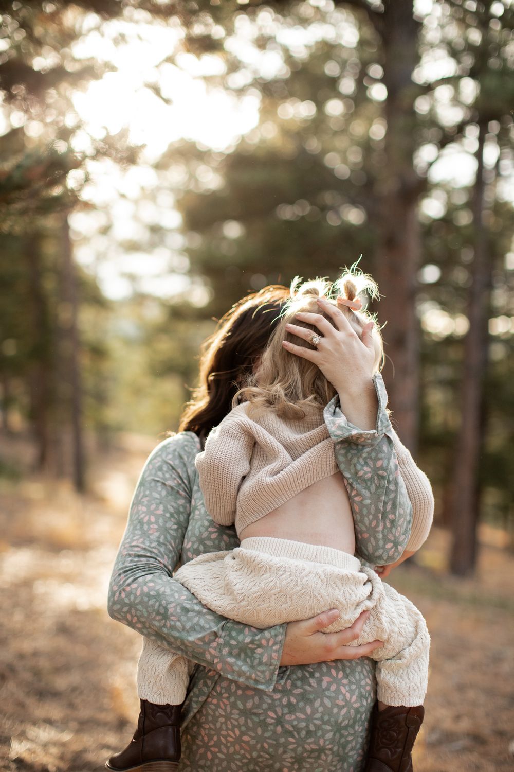 Tender embrace captured in golden sunlight filtering through forest trees, wearing cozy knit sweaters on an autumn day.