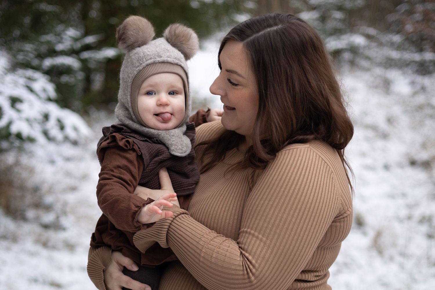 Two people dressed in warm winter clothing share a tender moment outdoors in a snowy setting.