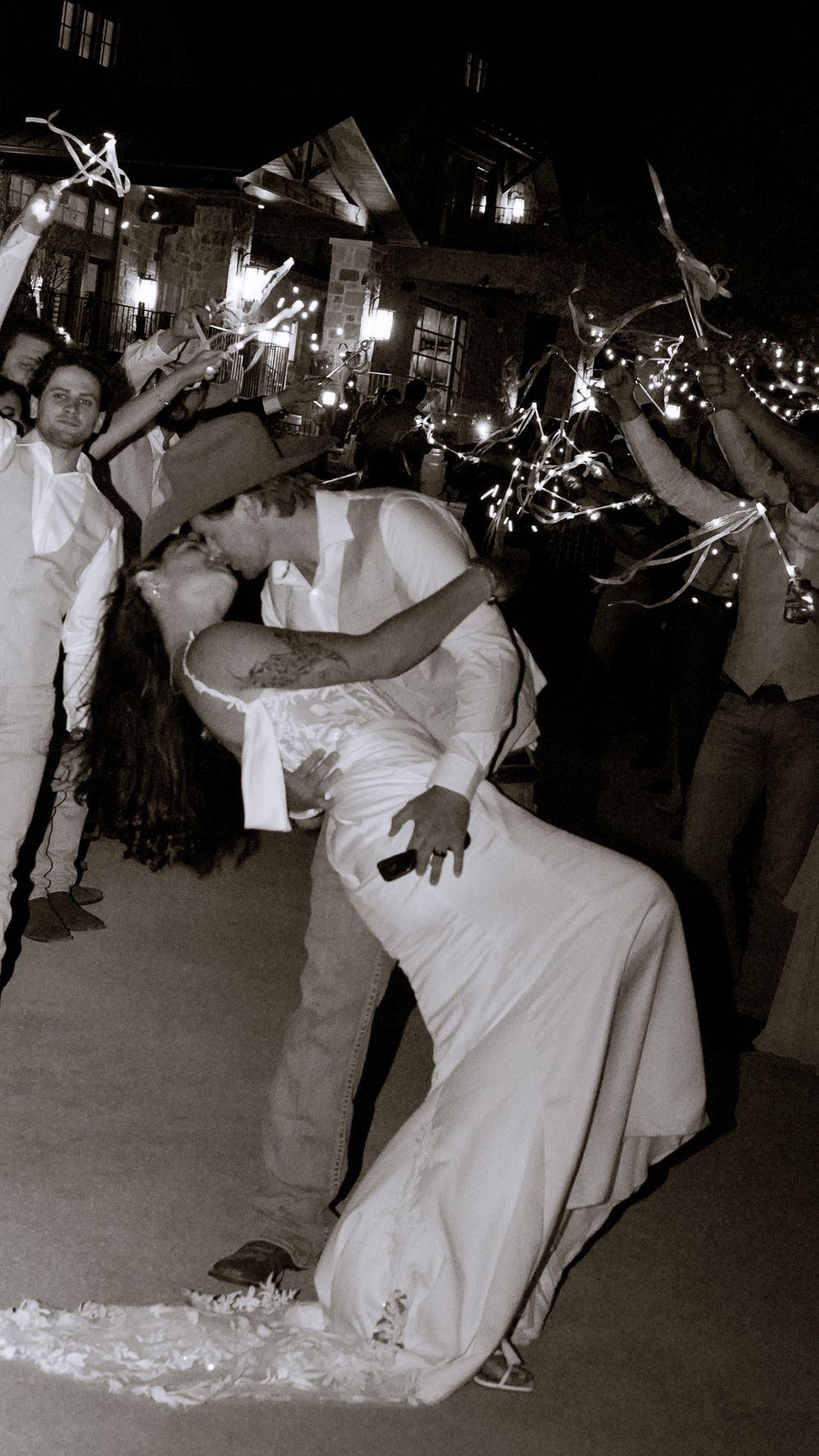 Bride and groom share dramatic dip kiss during sparkler send-off at nighttime wedding celebration.