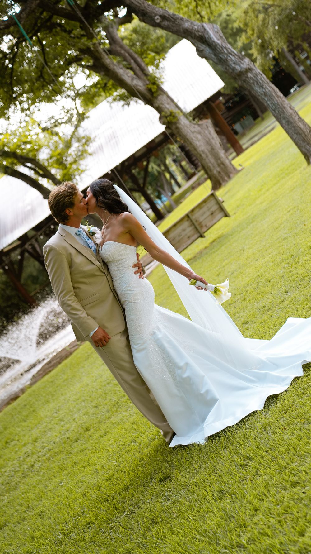 A bride and groom share a romantic kiss on a lush green lawn during their outdoor wedding ceremony.