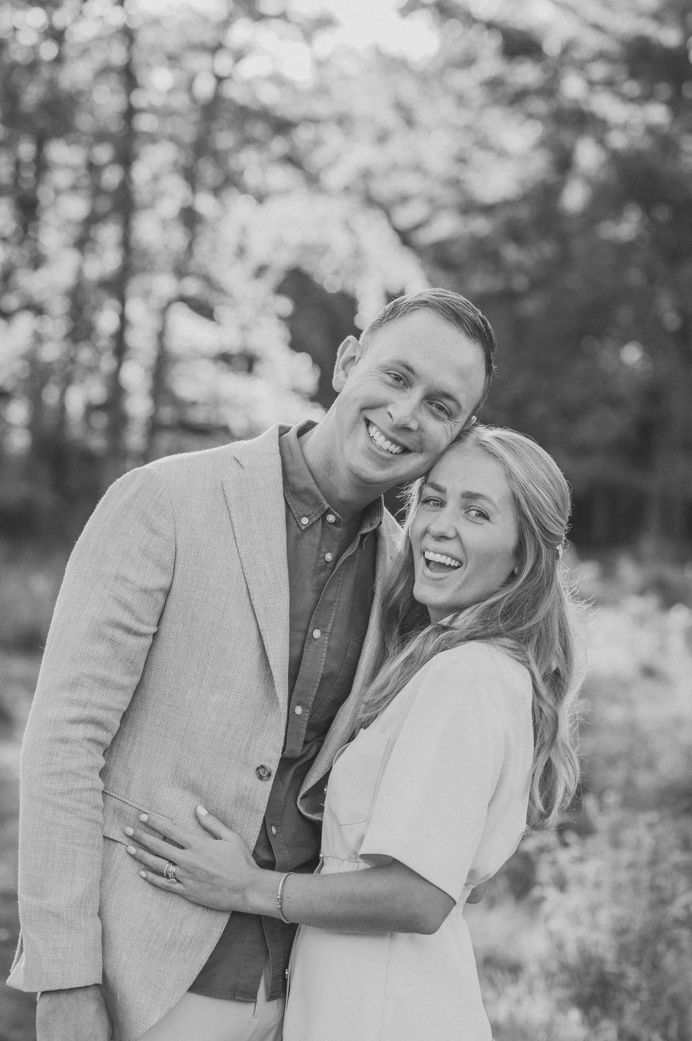 A joyful couple embracing and laughing together outdoors in a black and white portrait photo.
