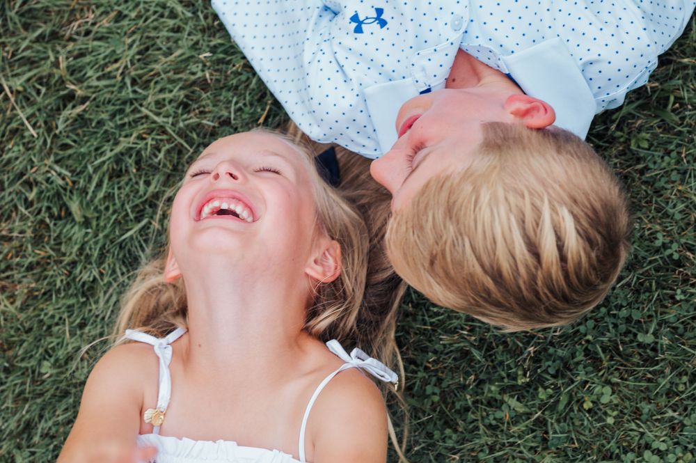 Two friends lying on grass outdoors and laughing together joyfully on a sunny day.