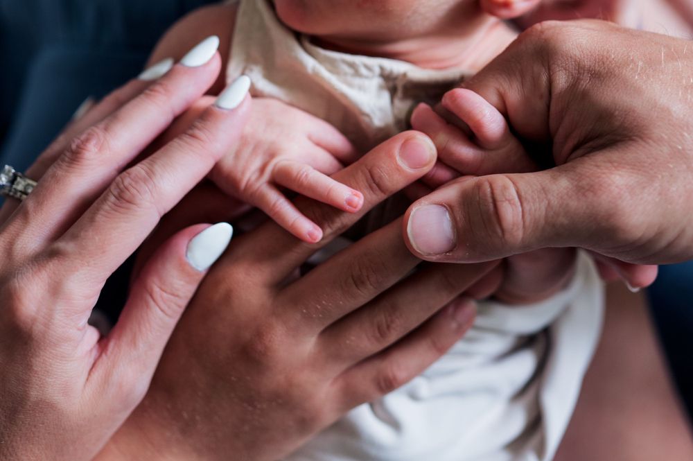 Close-up view of hands tenderly holding a tiny baby's fingers against white clothing.