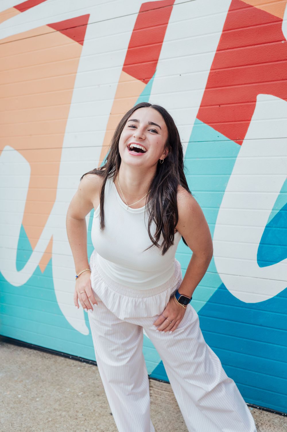 A joyful moment captured against a colorful geometric mural wall in white, coral and turquoise tones. senior portrait