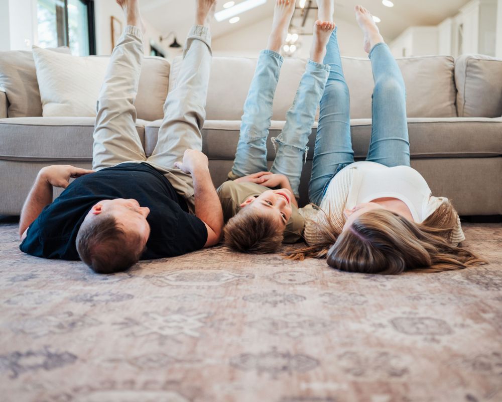 Family members lie on carpet with feet up against sofa in a relaxed, playful moment at home.