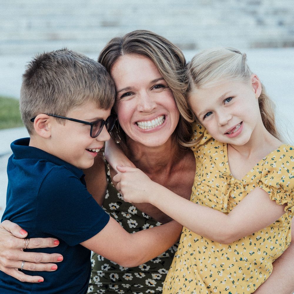 Happy moment shared between two children with woman, all embracing and laughing together outdoors.