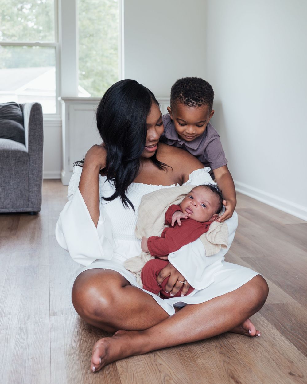 A tender family moment shared on hardwood floors in a bright interior space, as they gather around a newborn baby.