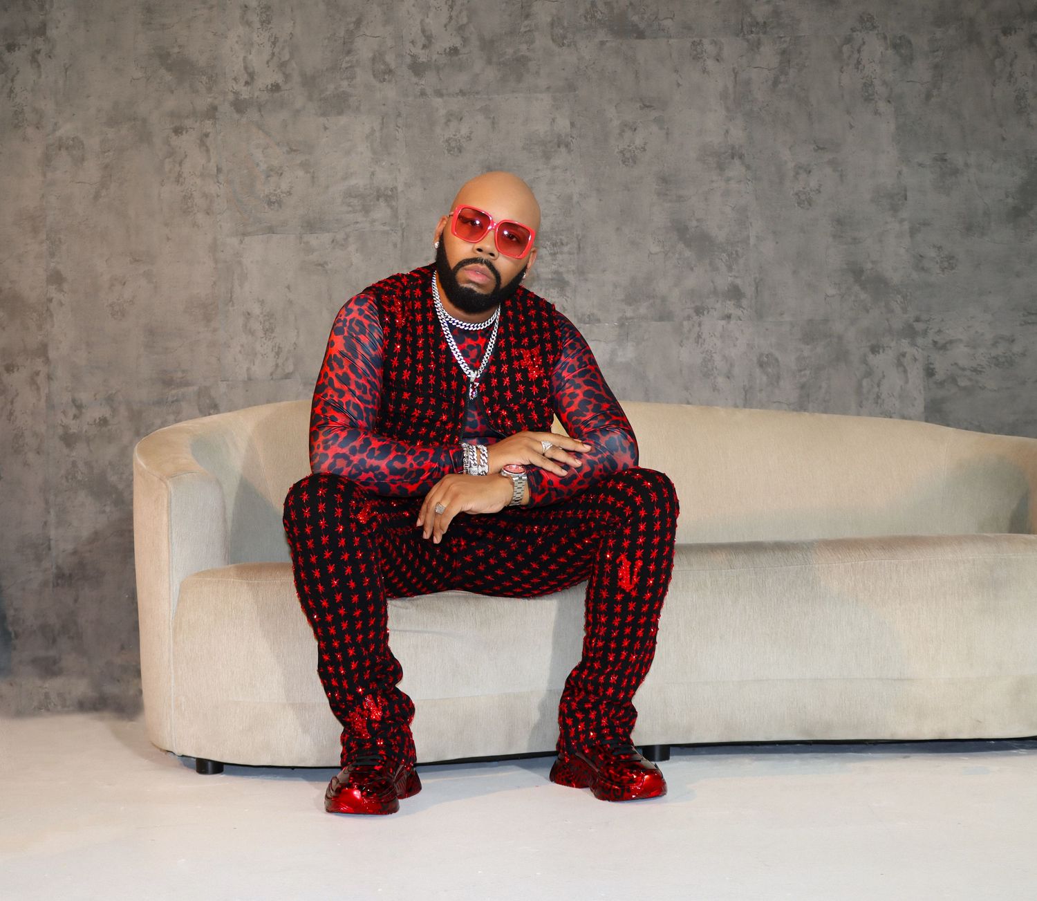 Person wearing red-patterned matching outfit and sneakers sitting on a white couch against a gray textured wall.