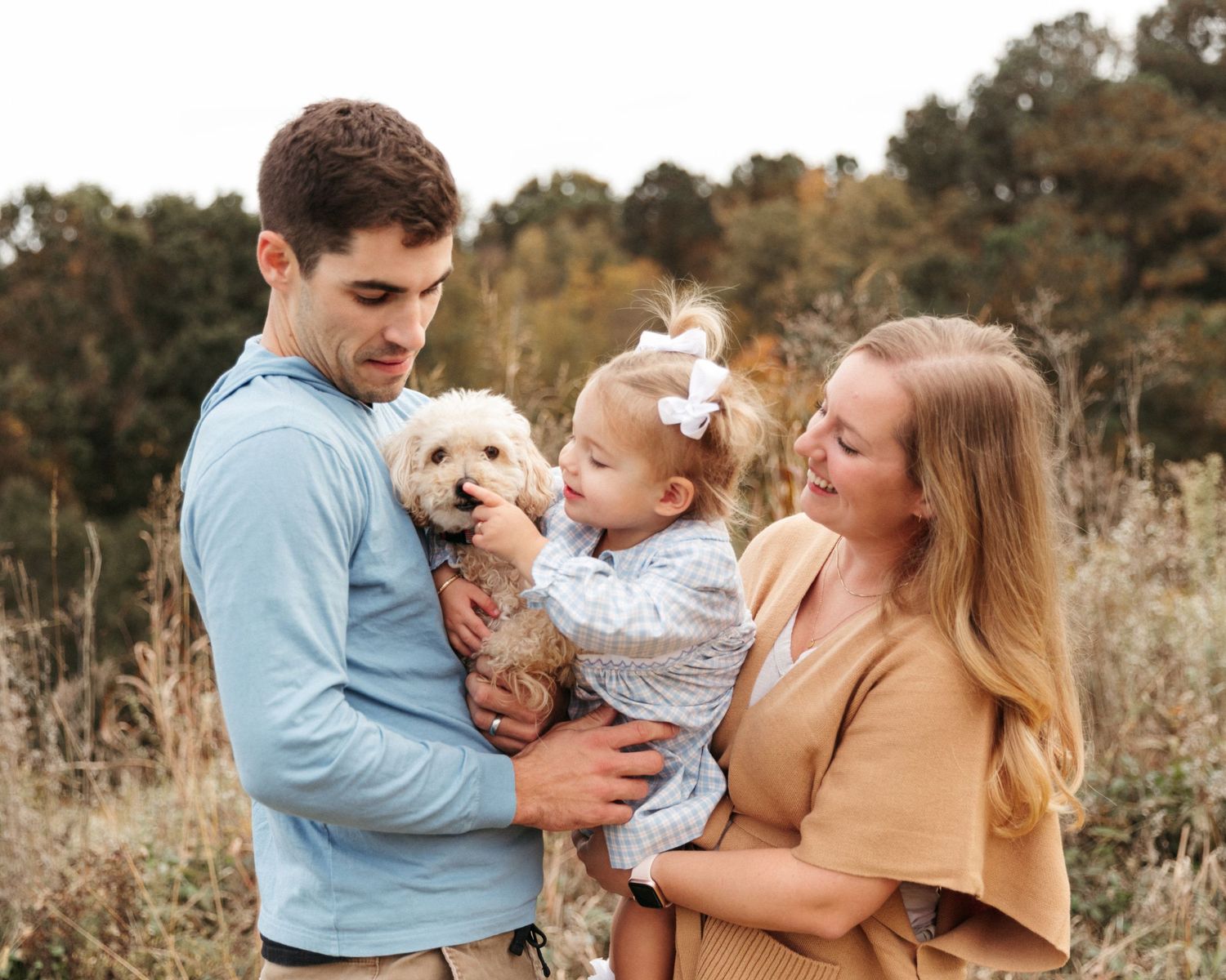 A sweet family moment captured outdoors against a natural backdrop in autumn colors. Little girl boops pet dogs nose.