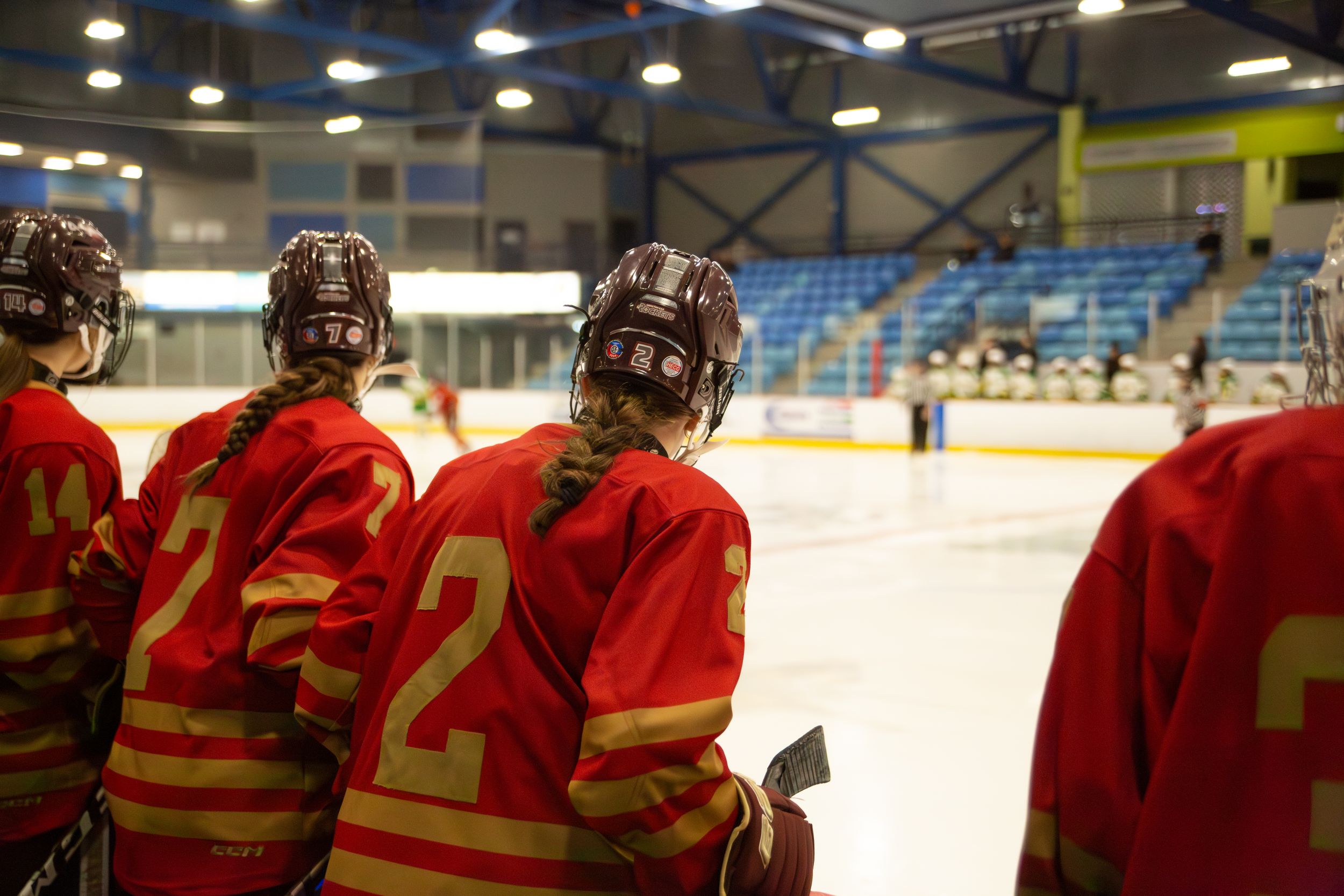 Hockey players in red jerseys sit on the bench watching the game from the sidelines.