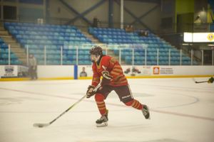 Hockey player in red uniform skating with stick on indoor rink during game action.