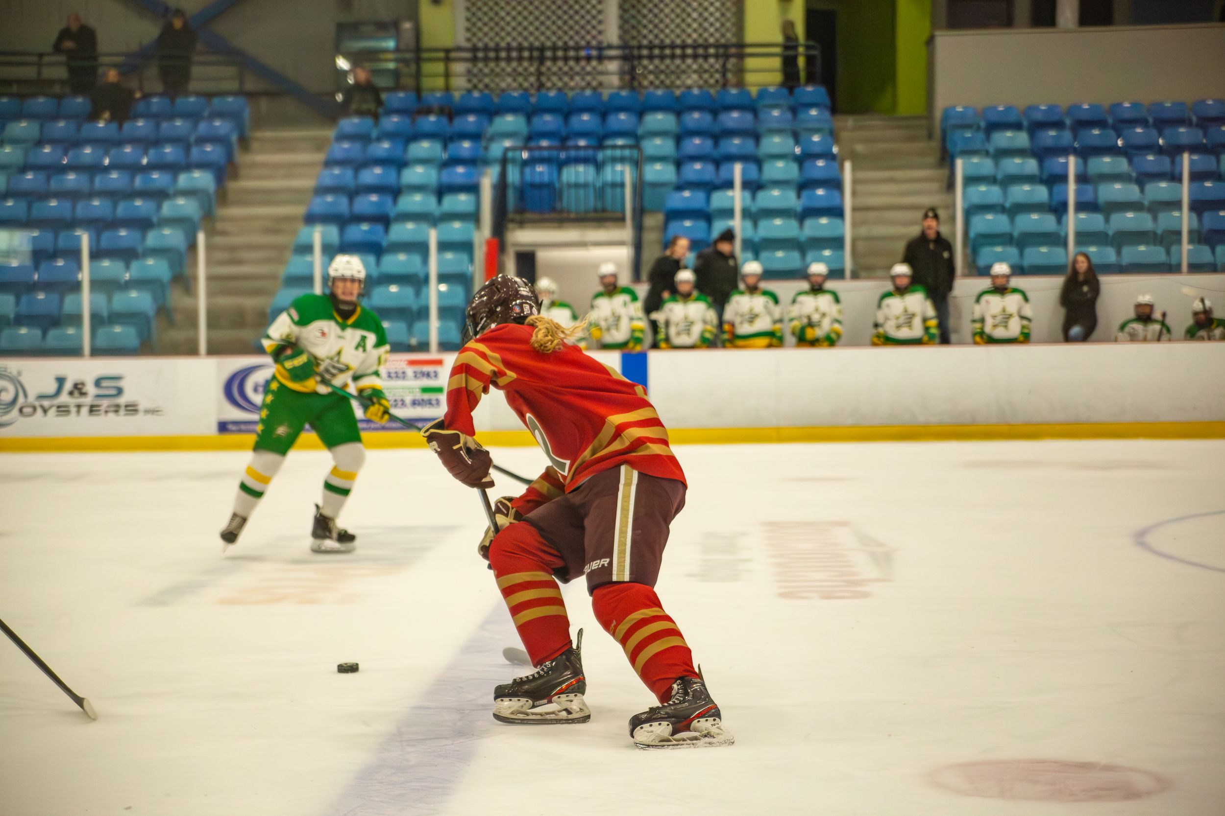 Hockey player in red uniform controls the puck while facing off against opponent in green.