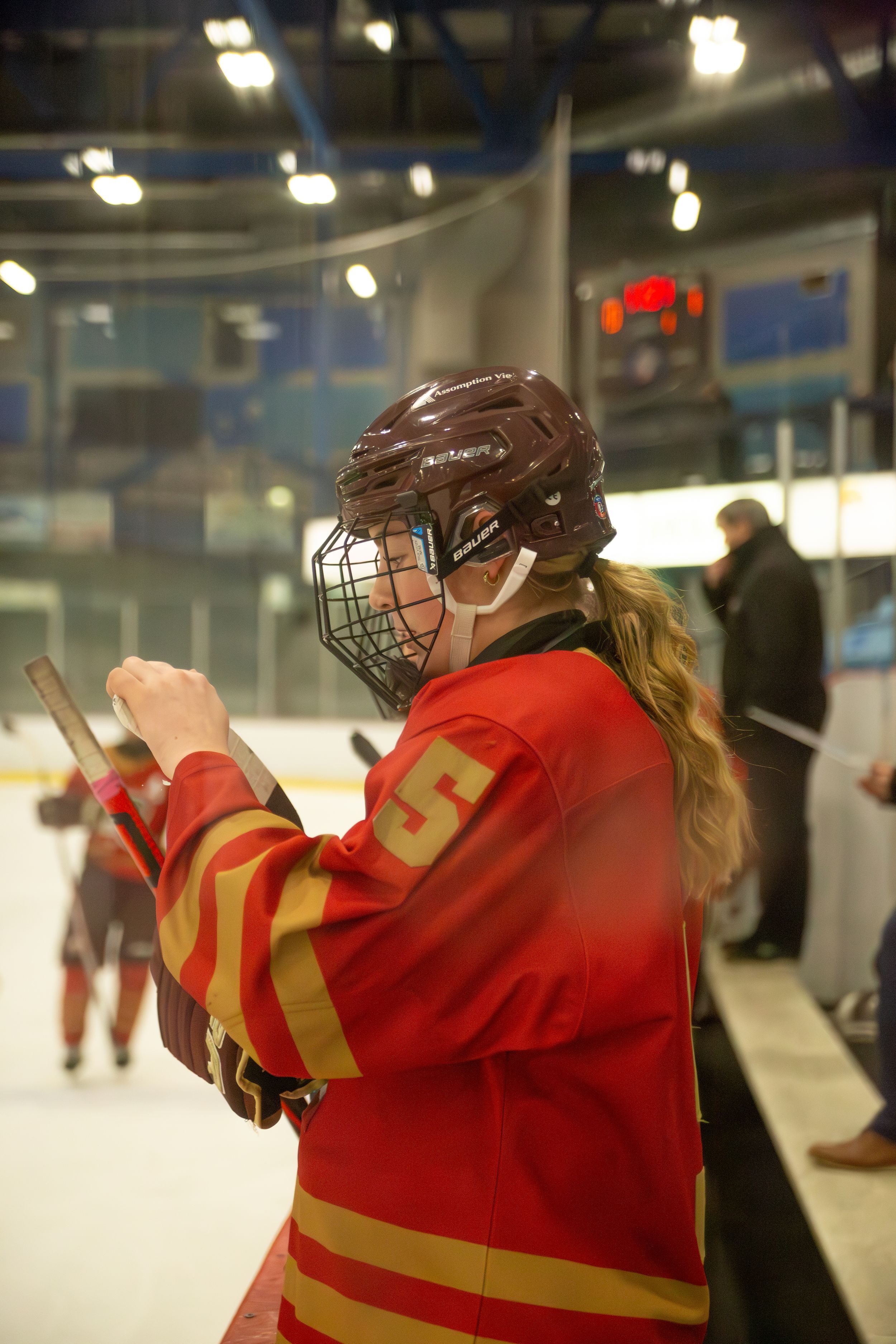 Hockey player in red uniform claps while standing near the rink boards.