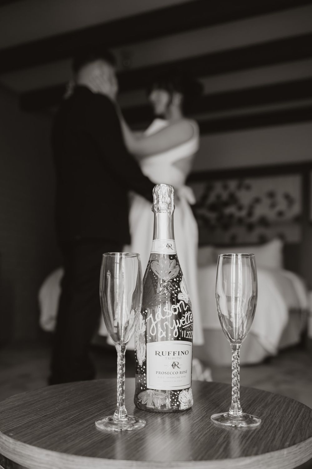 Champagne bottle and two flutes on table with dancing couple silhouette in background.