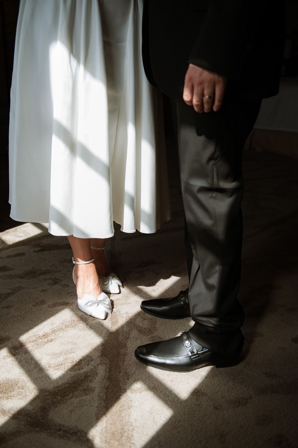 Contrasting formal shoes and attire of couple standing in dramatic window light.