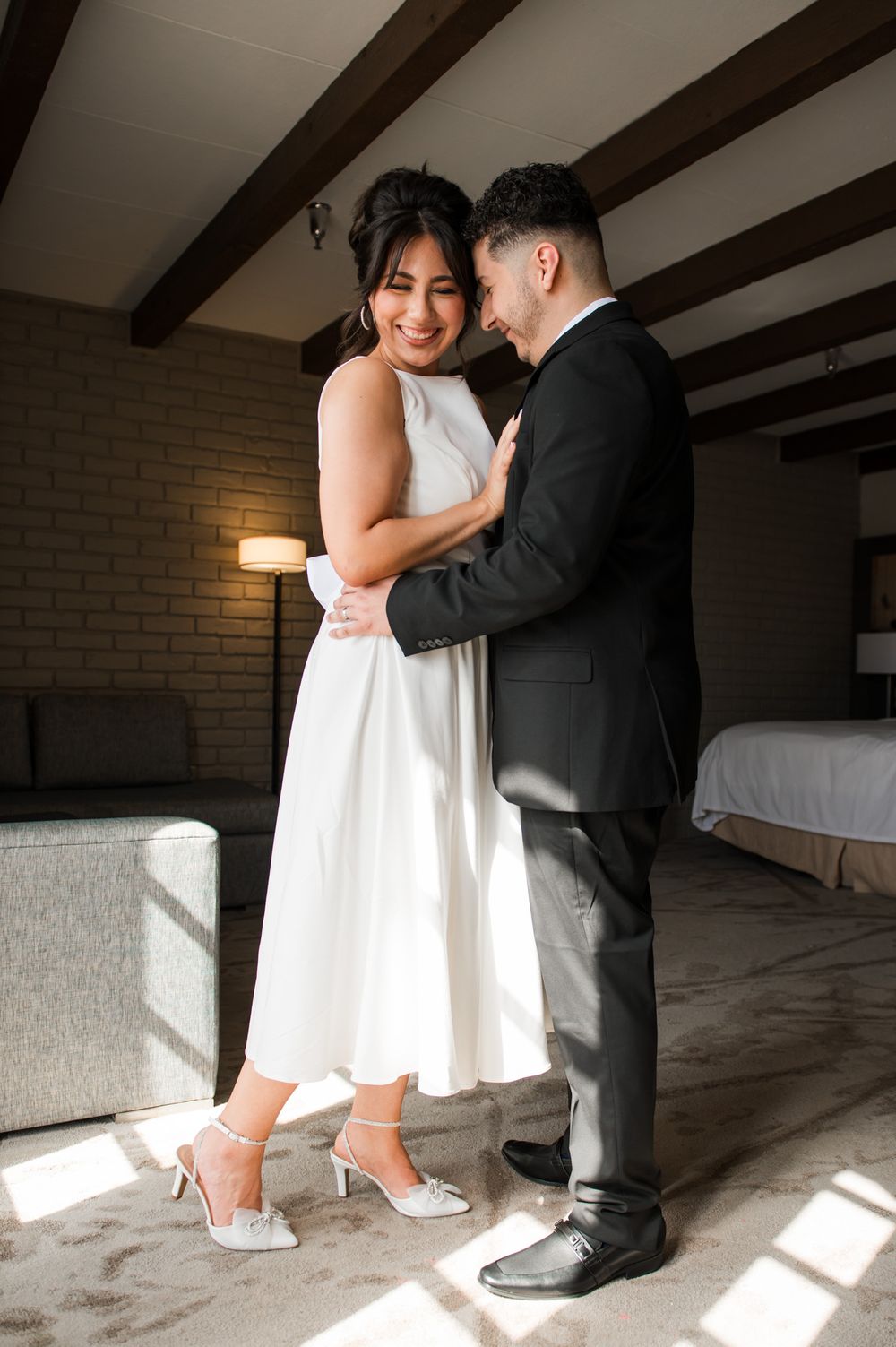 Wedding couple in elegant attire sharing intimate moment in sunlit room.