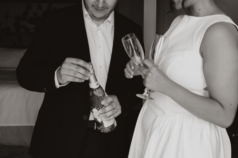 Black and white photo of couple toasting with champagne glasses at wedding celebration.