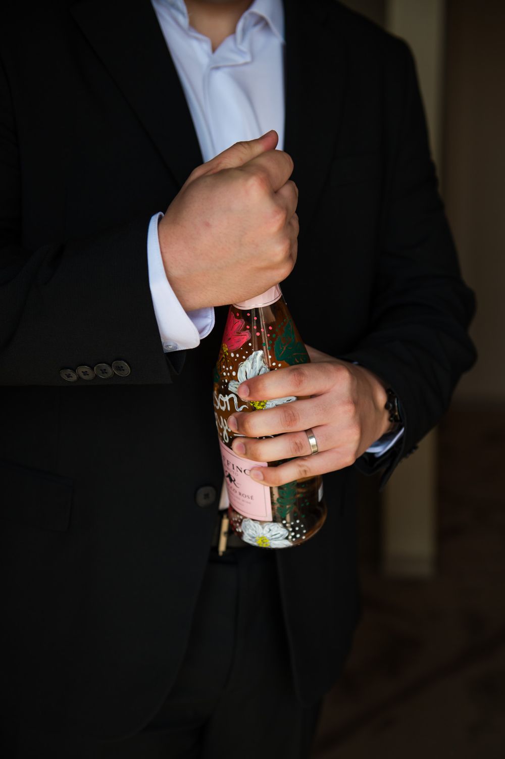 Close-up of hands holding decorated champagne bottle in formal wedding attire.