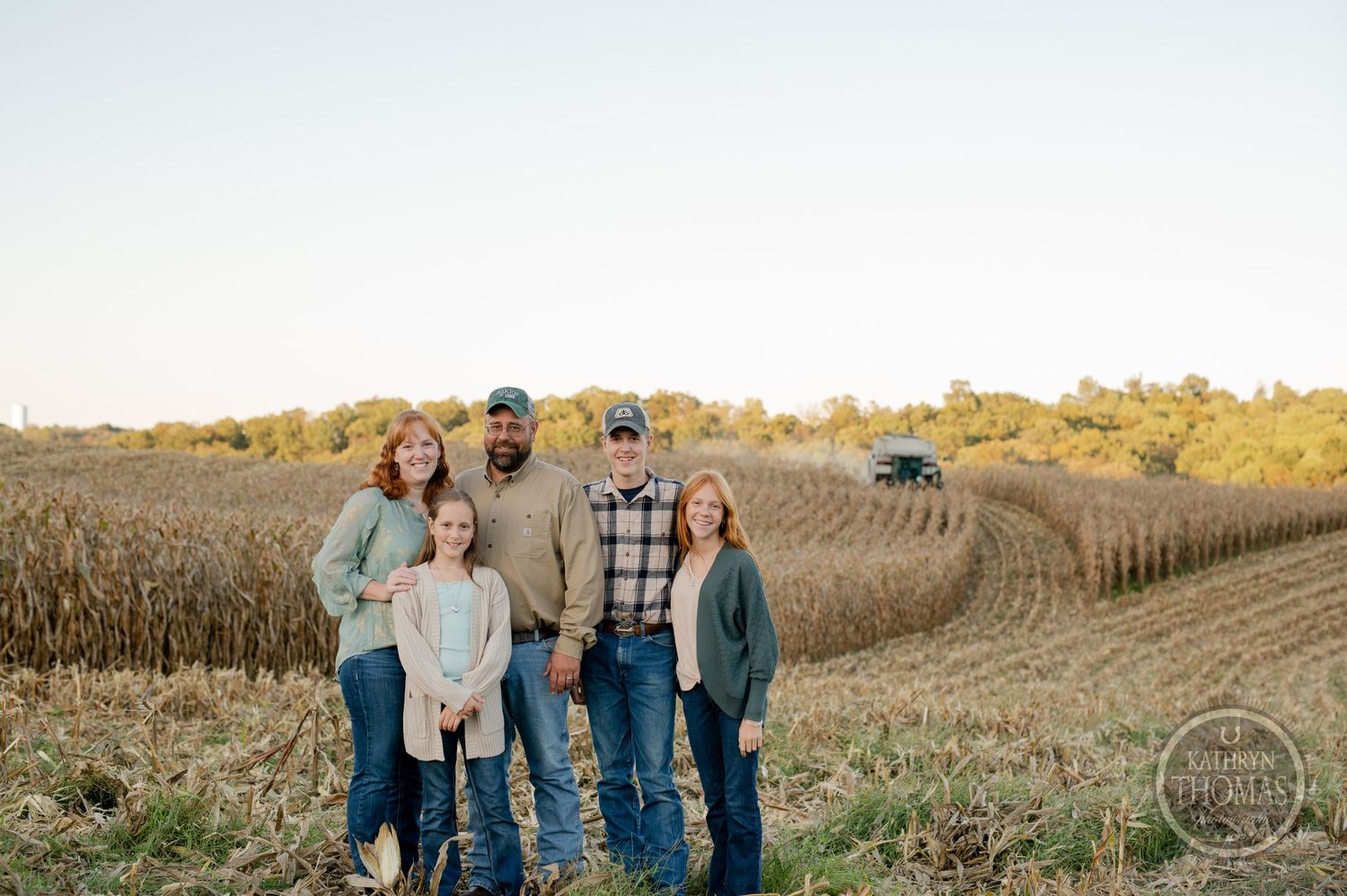 Family standing together in a harvested farm field at sunset.