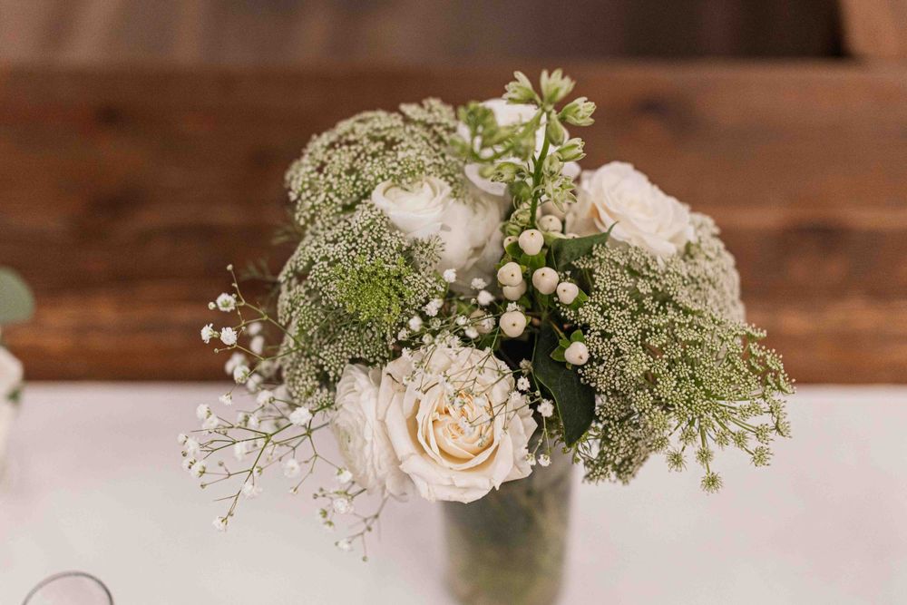 Elegant wedding centerpiece with cream roses, baby's breath, and delicate greenery in a simple glass vase.