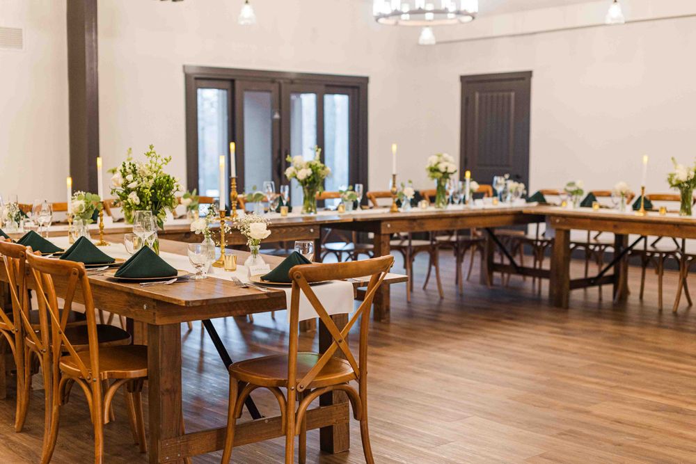 Rustic wedding reception venue with wooden farmhouse tables, crossback chairs and formal place settings.