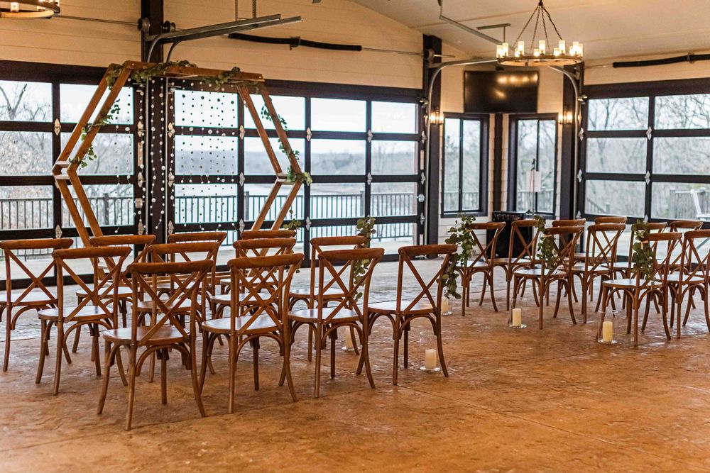Empty waterfront restaurant interior with wooden cross-back chairs and large windows overlooking scenic water view.