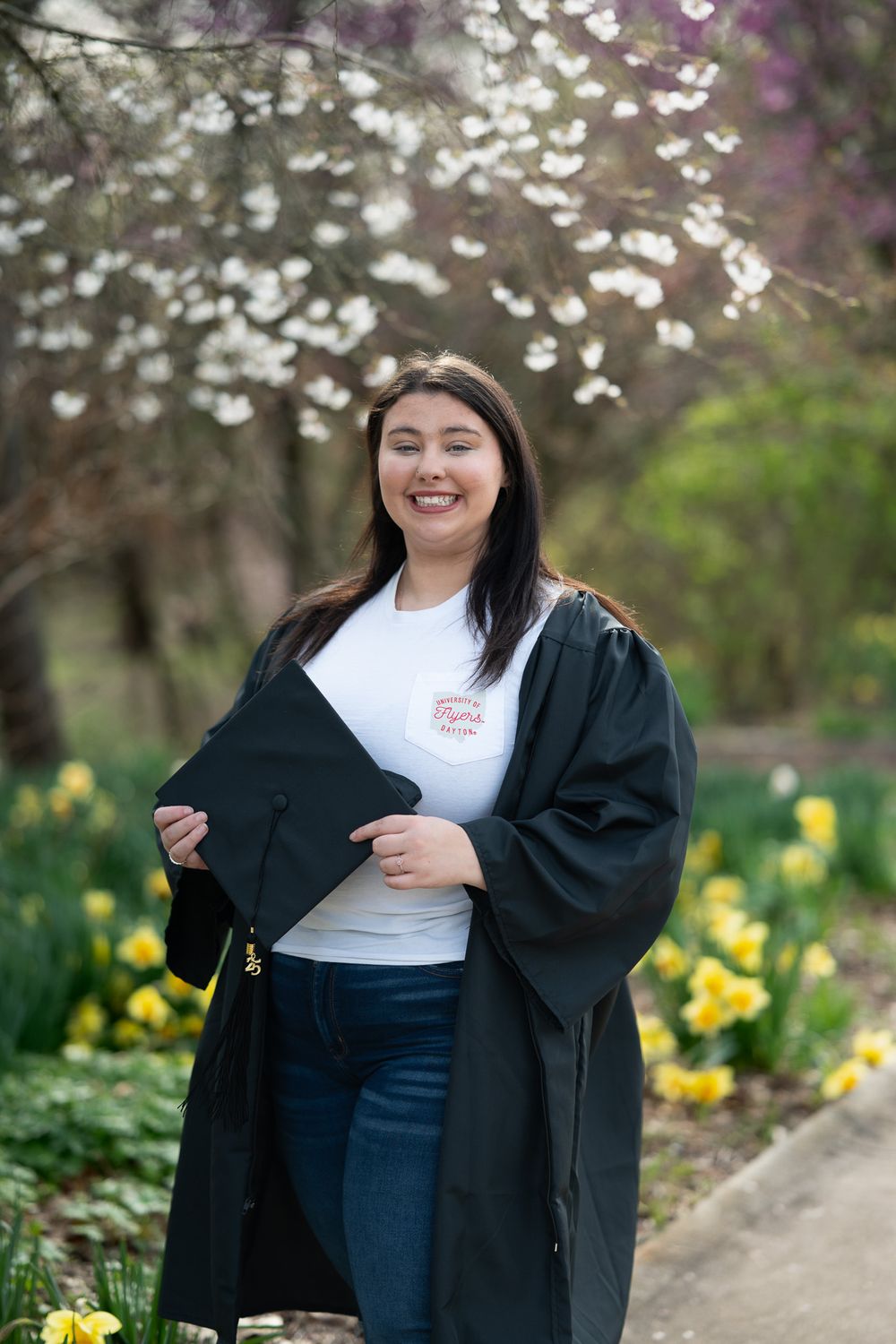 Graduate in black gown posing with cherry blossoms and daffodils.