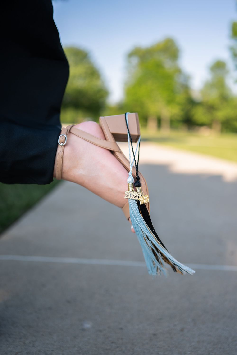 Hand holding a graduation cap with blue tassel and 2024 charm outdoors.