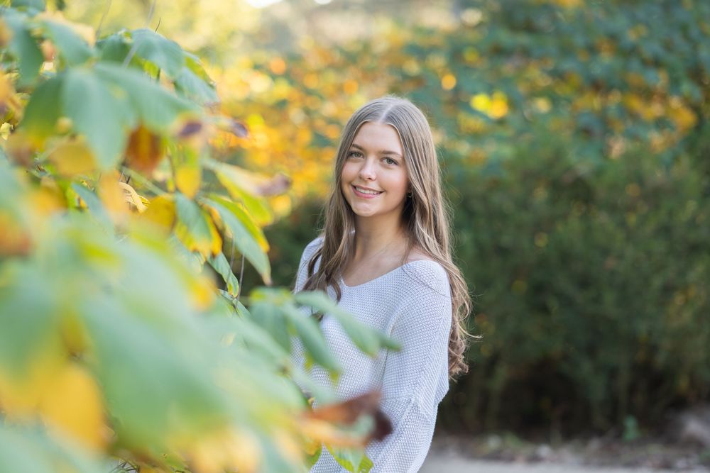 A person poses playfully among yellow autumn leaves during a fall outdoor photo session.