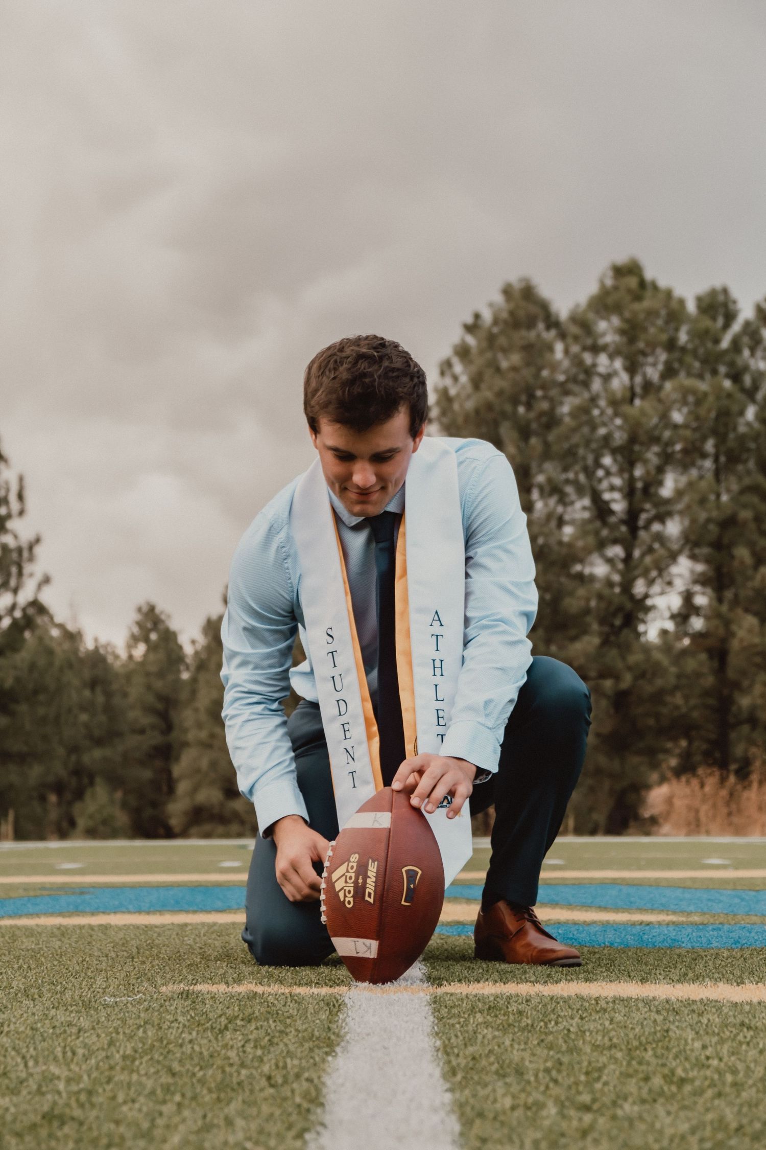 Senior portrait photographer captures sequence of football placement on field in light blue dress shirt.