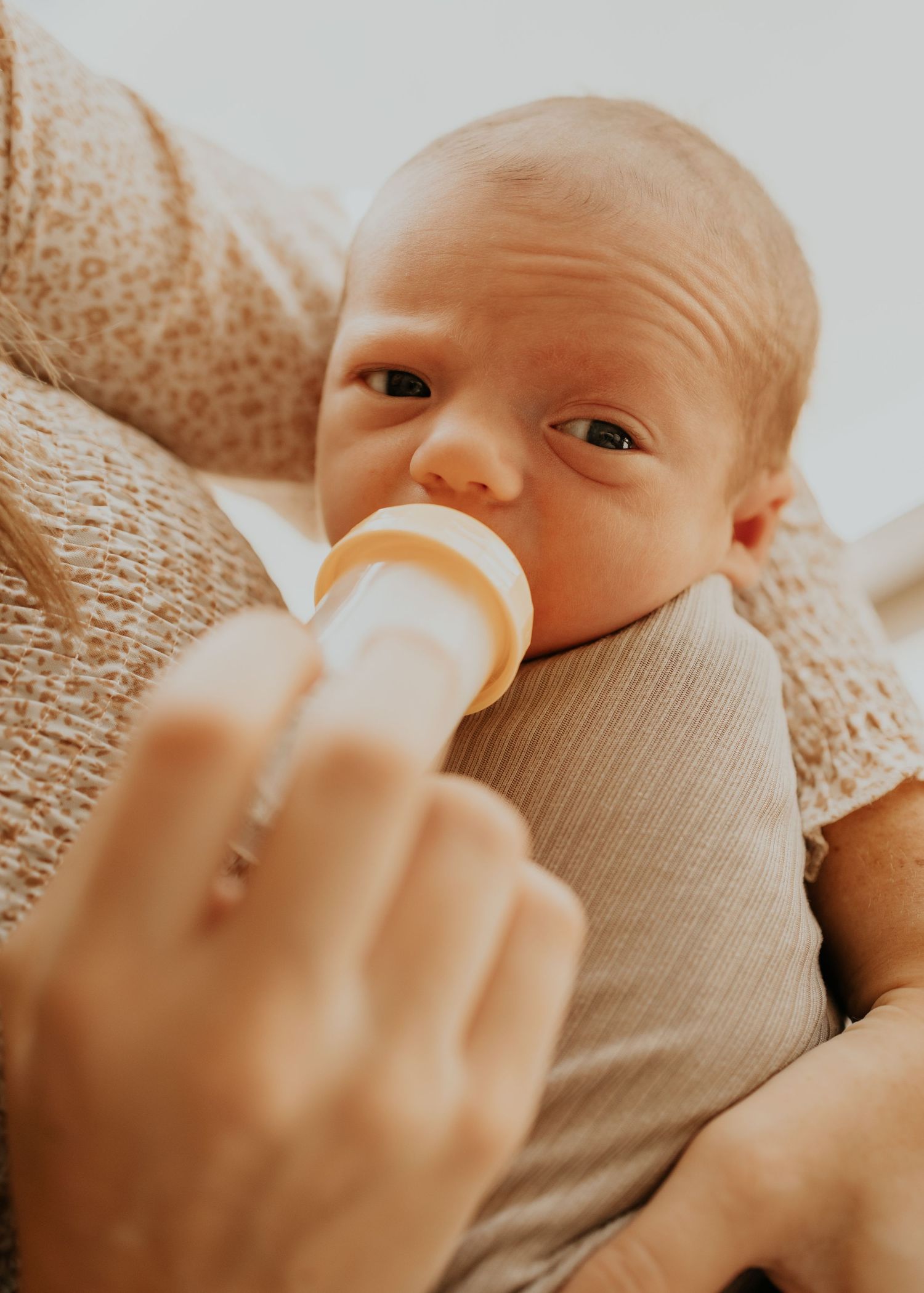 A baby lying on soft fabric while being bottle fed in warm lighting.