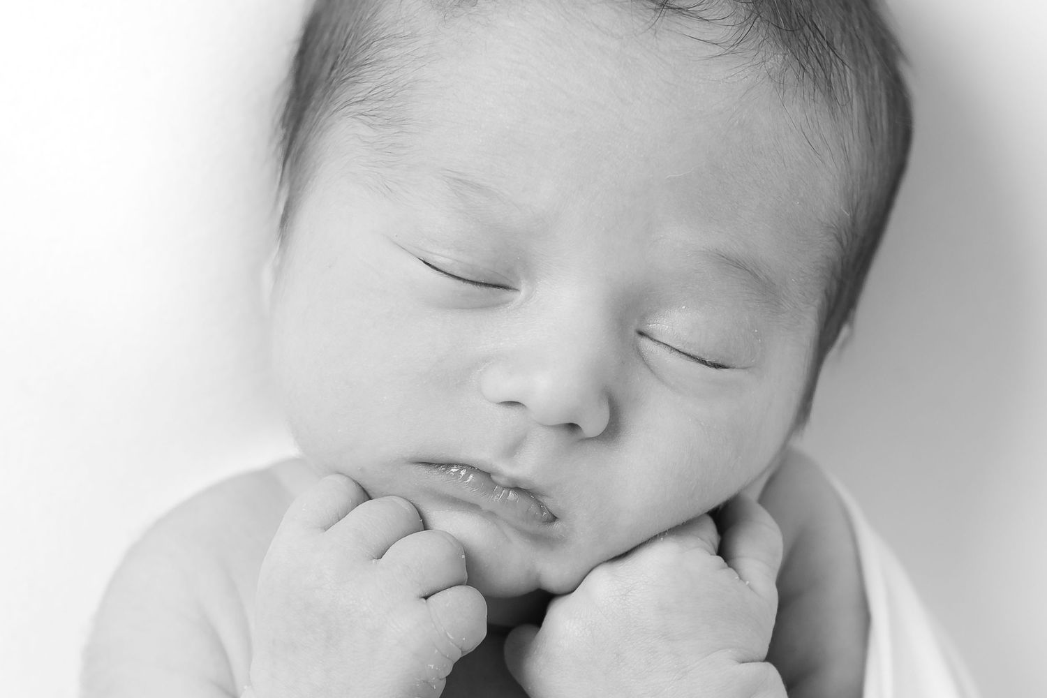 Peaceful black and white portrait of sleeping newborn with hand near face.