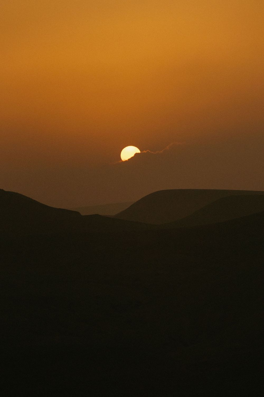 Golden sunset over silhouetted desert hills with the sun partially visible on the horizon.