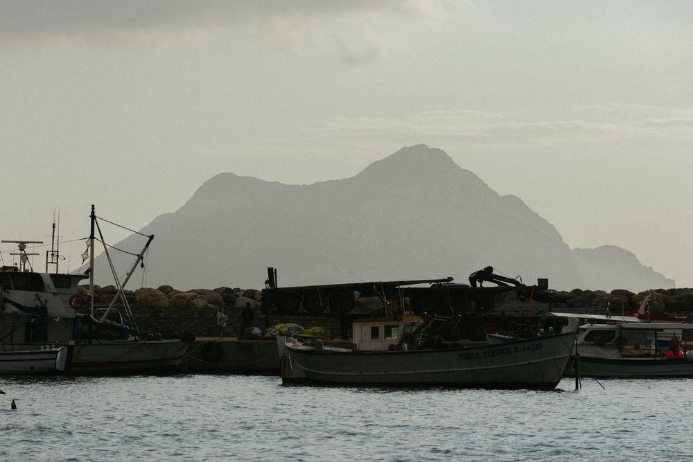 Fishing boats moored in a calm harbor with a dramatic mountain silhouette rising in the misty background.