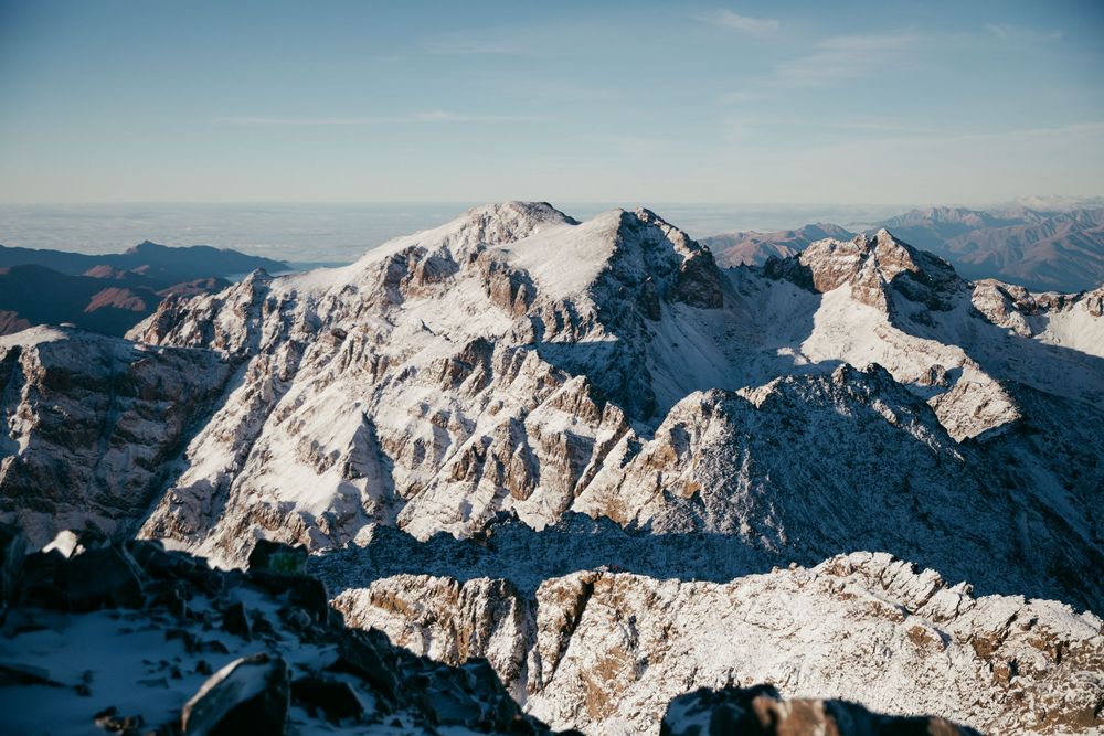 Snow-capped mountain peaks stretch across a panoramic winter landscape under a bright blue sky.