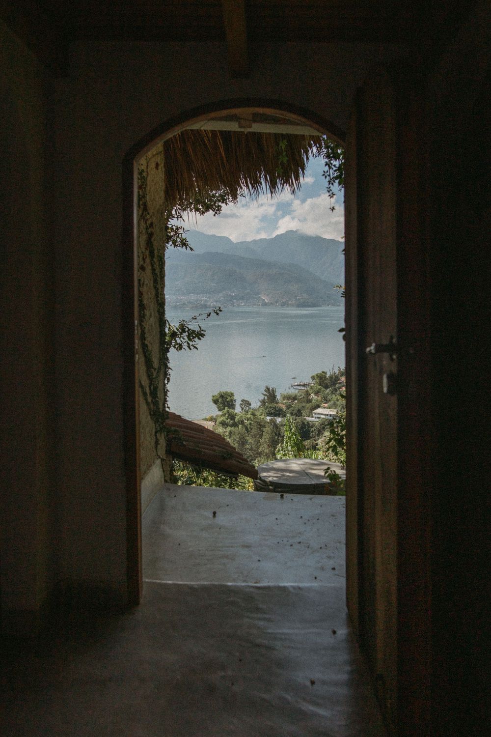 View through a dark archway opening to a scenic mountain lake landscape with trees and natural lighting.