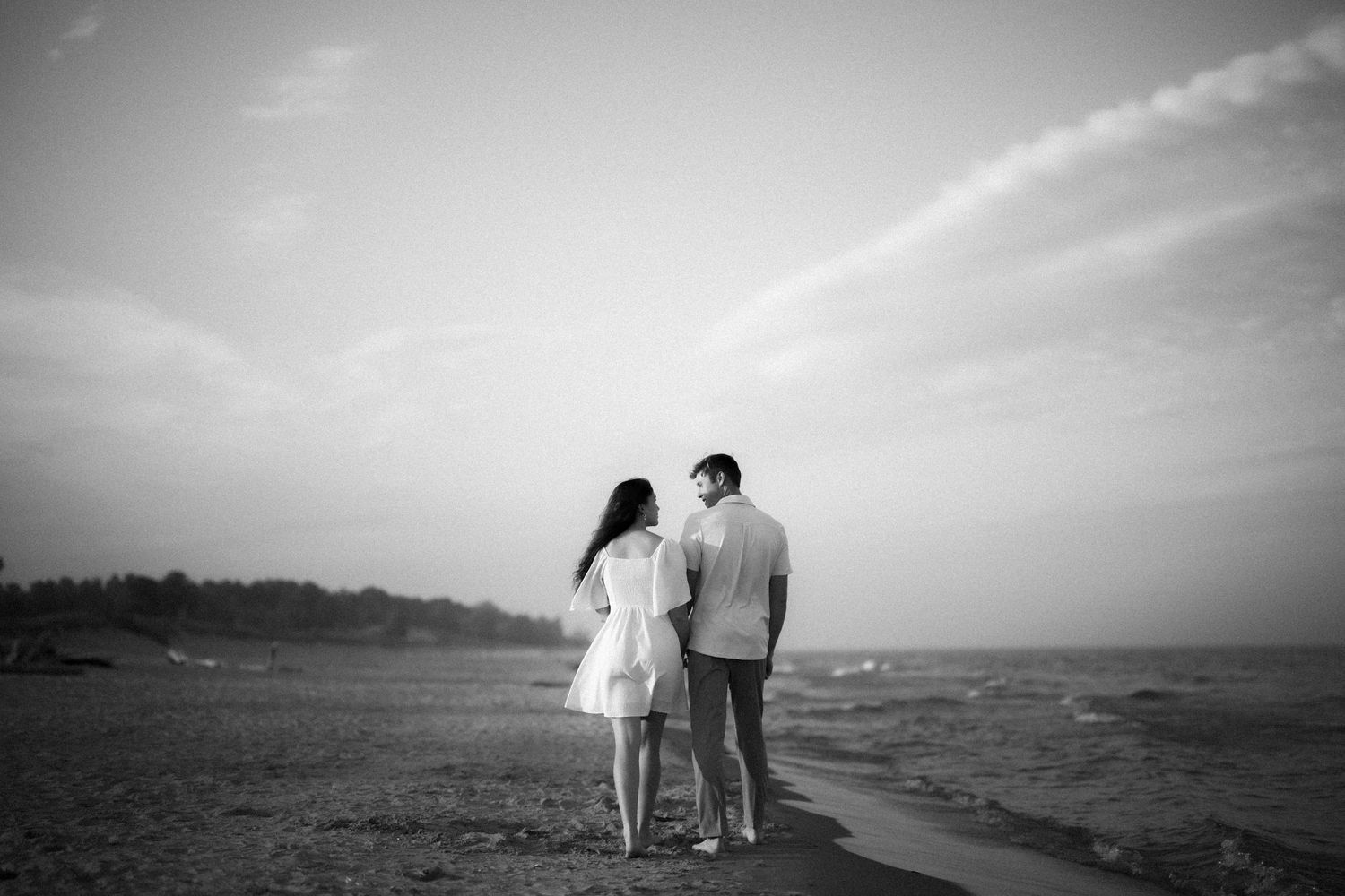 A couple stands close together on a beach at dusk in black and white silhouette.