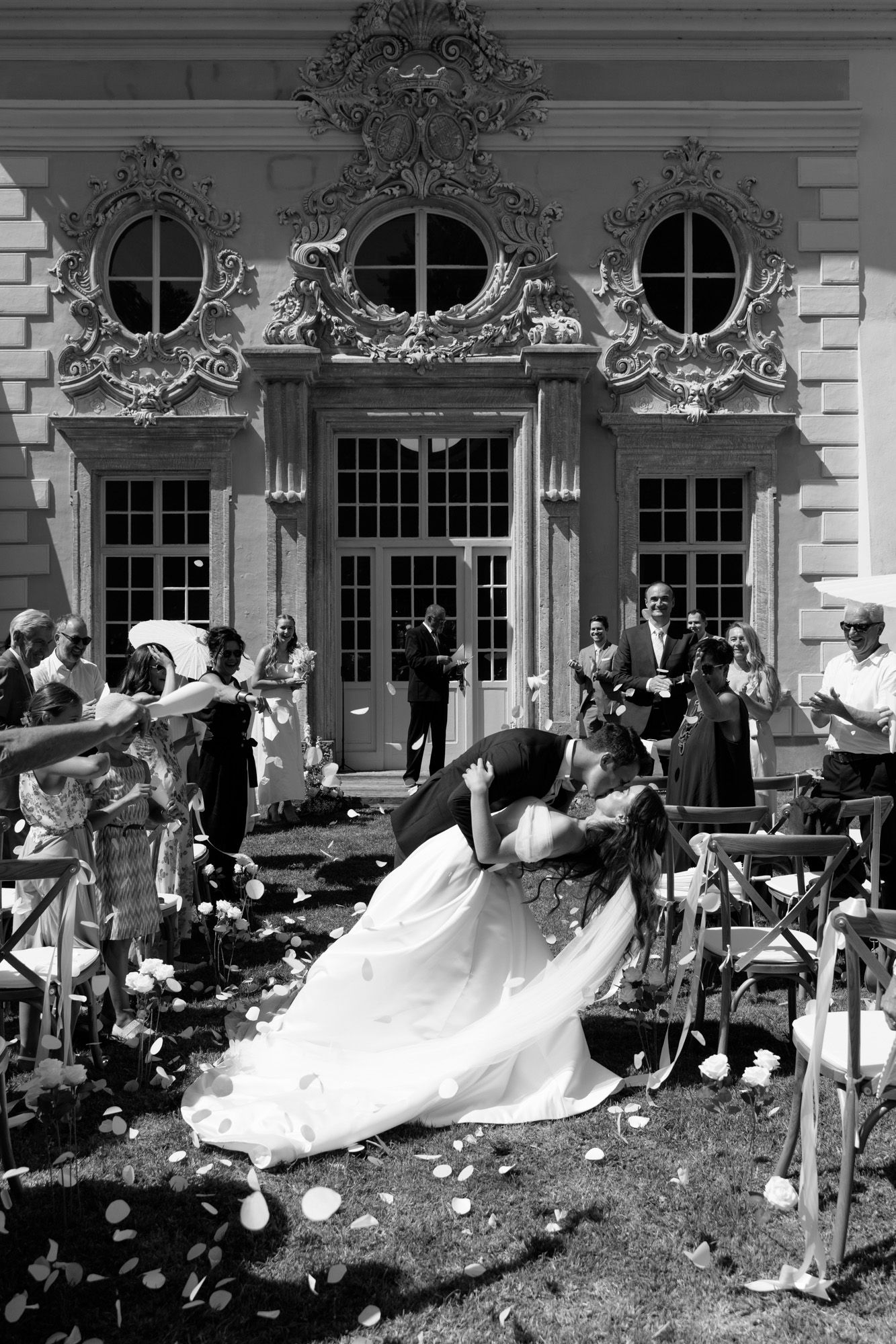 A romantic dip kiss captured outside an ornate building during a wedding celebration.