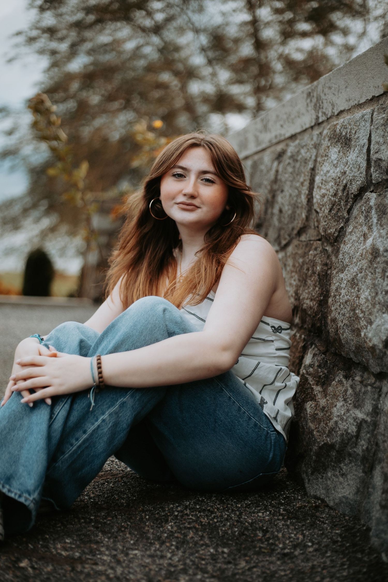 A person in casual denim sits against a stone wall outdoors during golden hour.