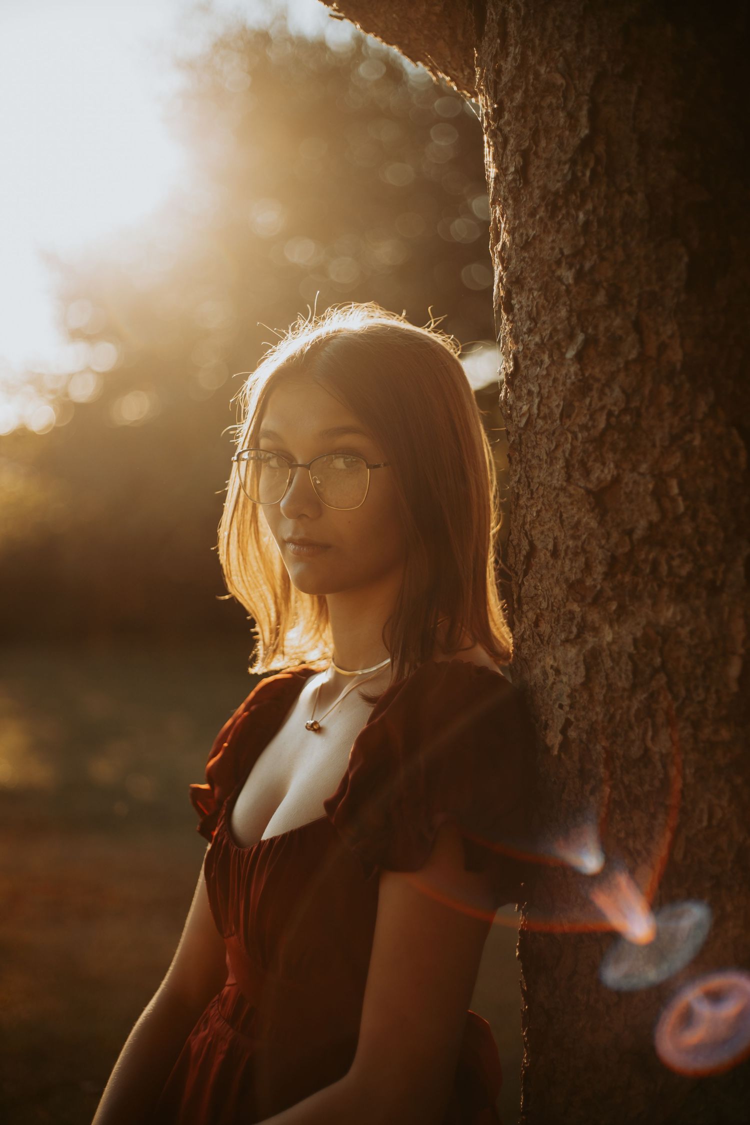 Person in warm sunset light leaning against tree trunk while smoking creates atmospheric silhouette effect.