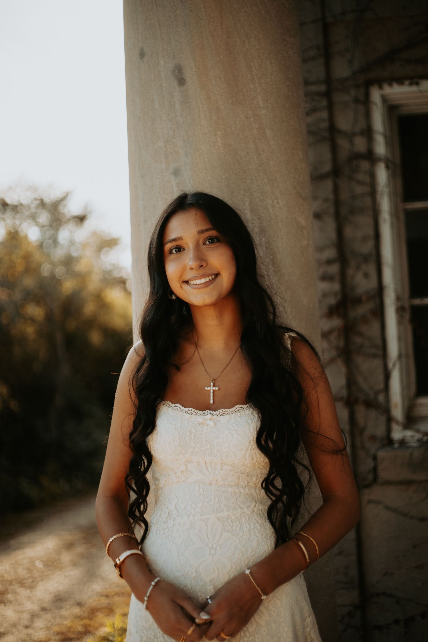 A bride in a white lace dress poses during a golden hour photoshoot with sunlight filtering through columns.