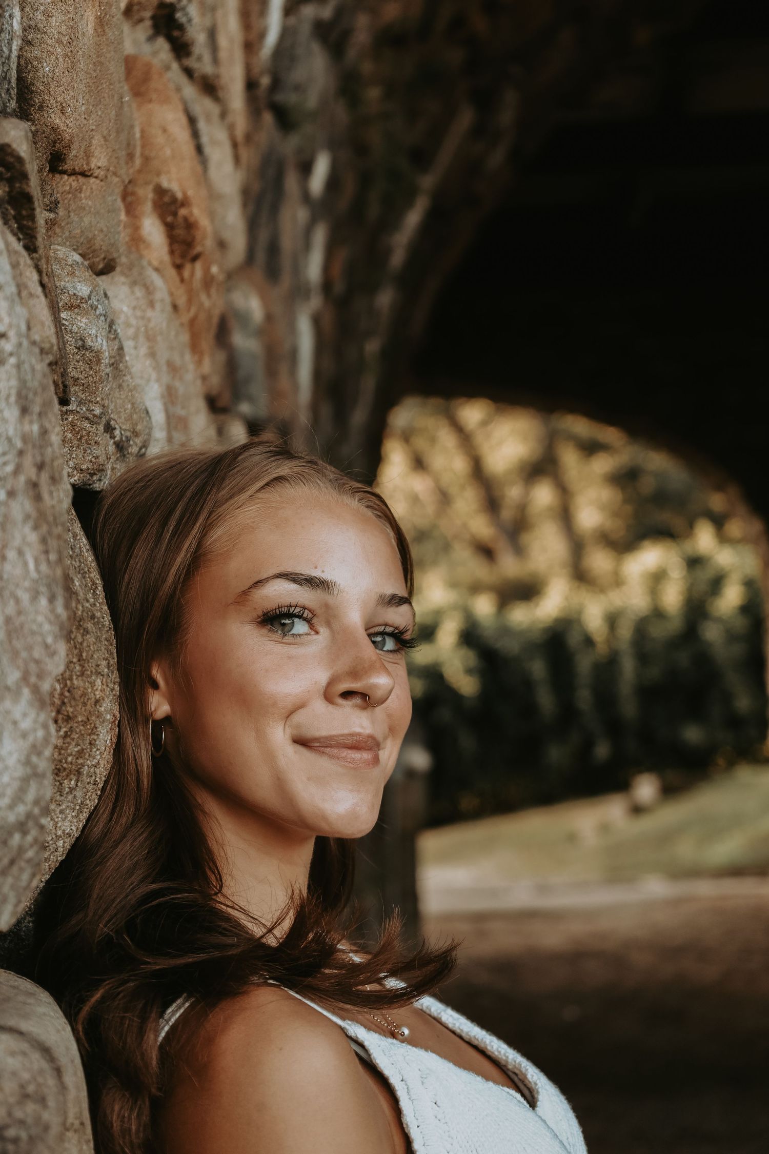A series of artistic portraits showing a warm smile and natural lighting against a rustic stone wall backdrop.