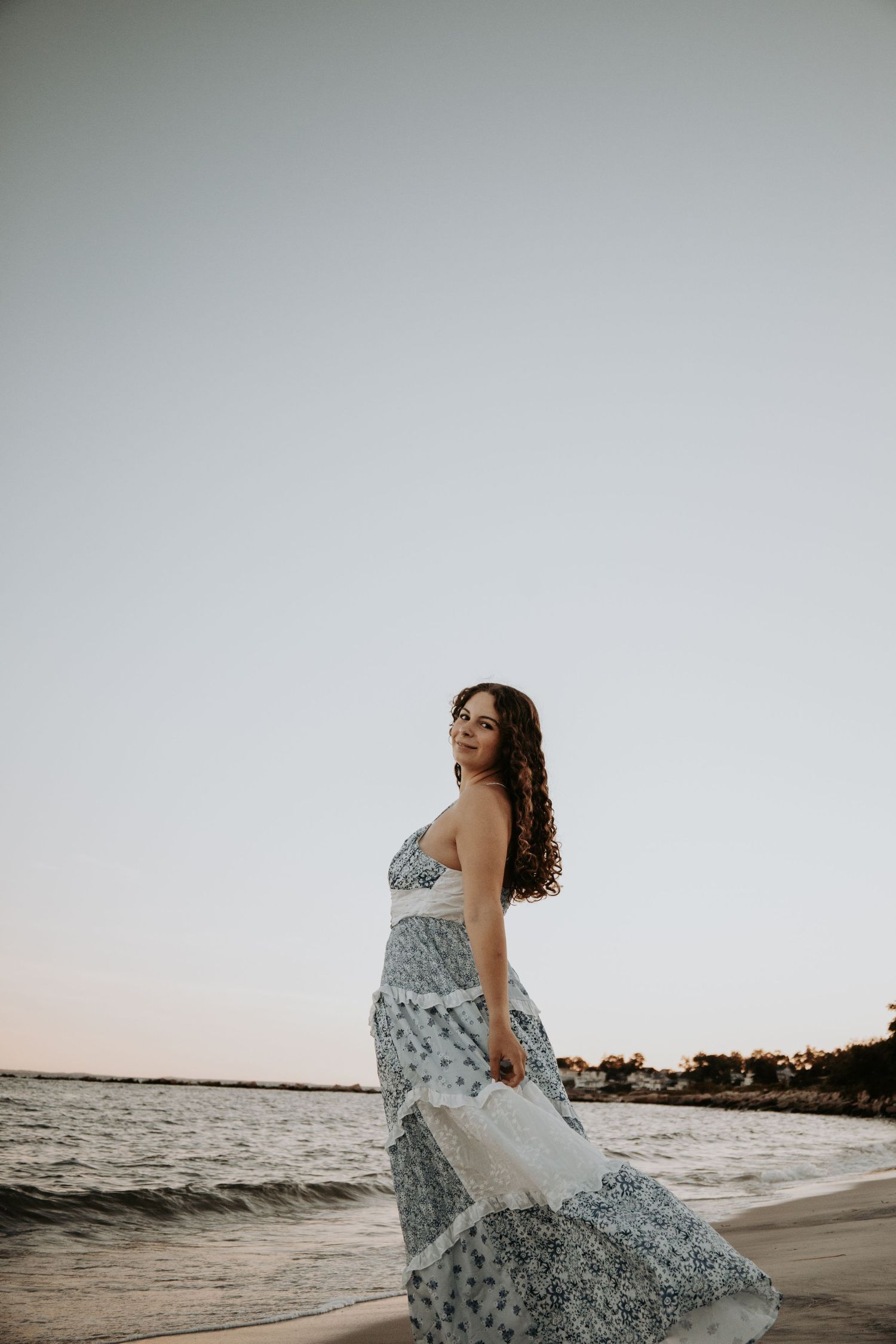 Woman in flowing floral dress twirls gracefully on beach at sunset as waves crash behind her in series of photos.