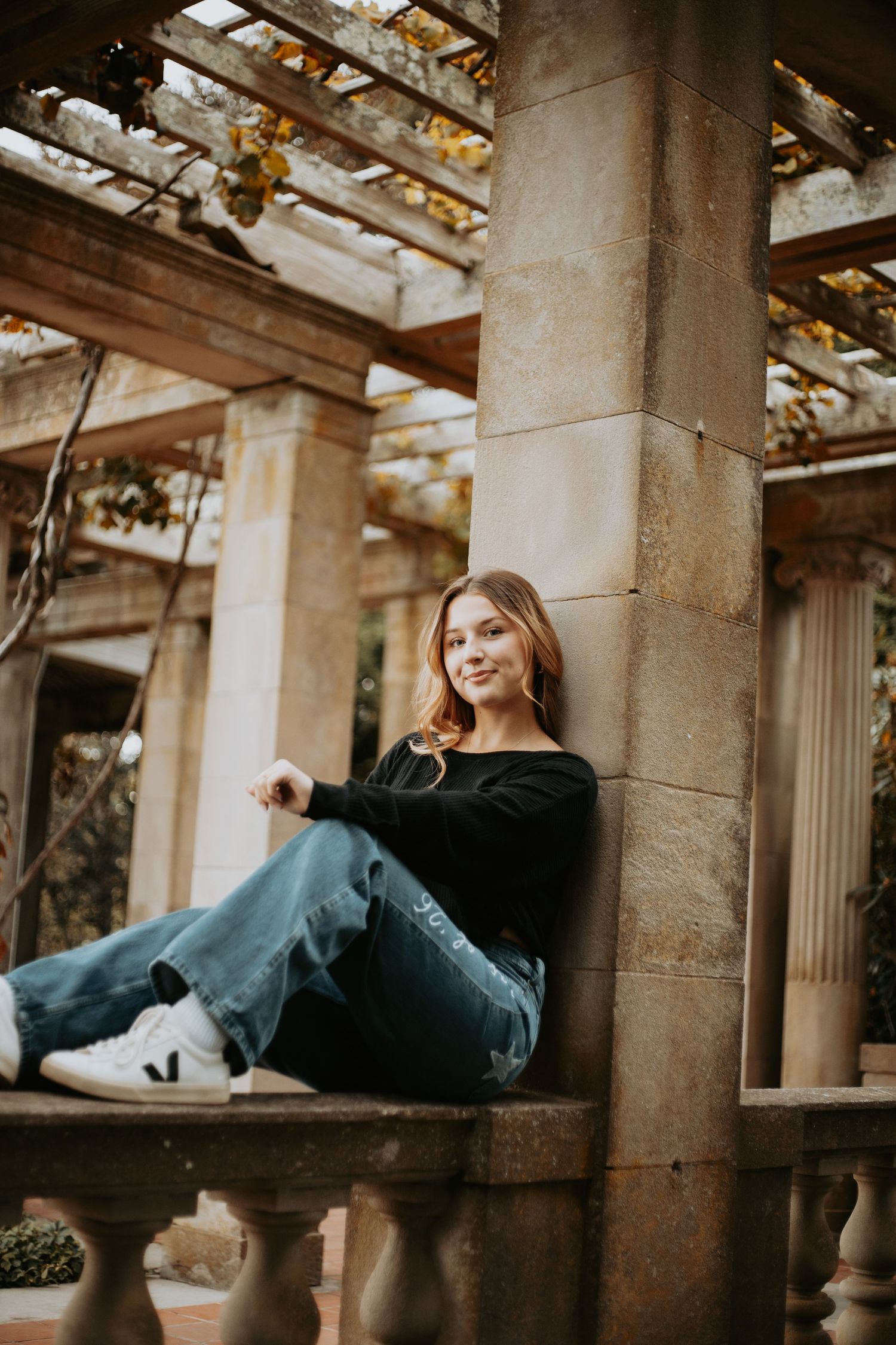 A person in casual wear leans against a stone pillar in an architectural space with natural lighting.