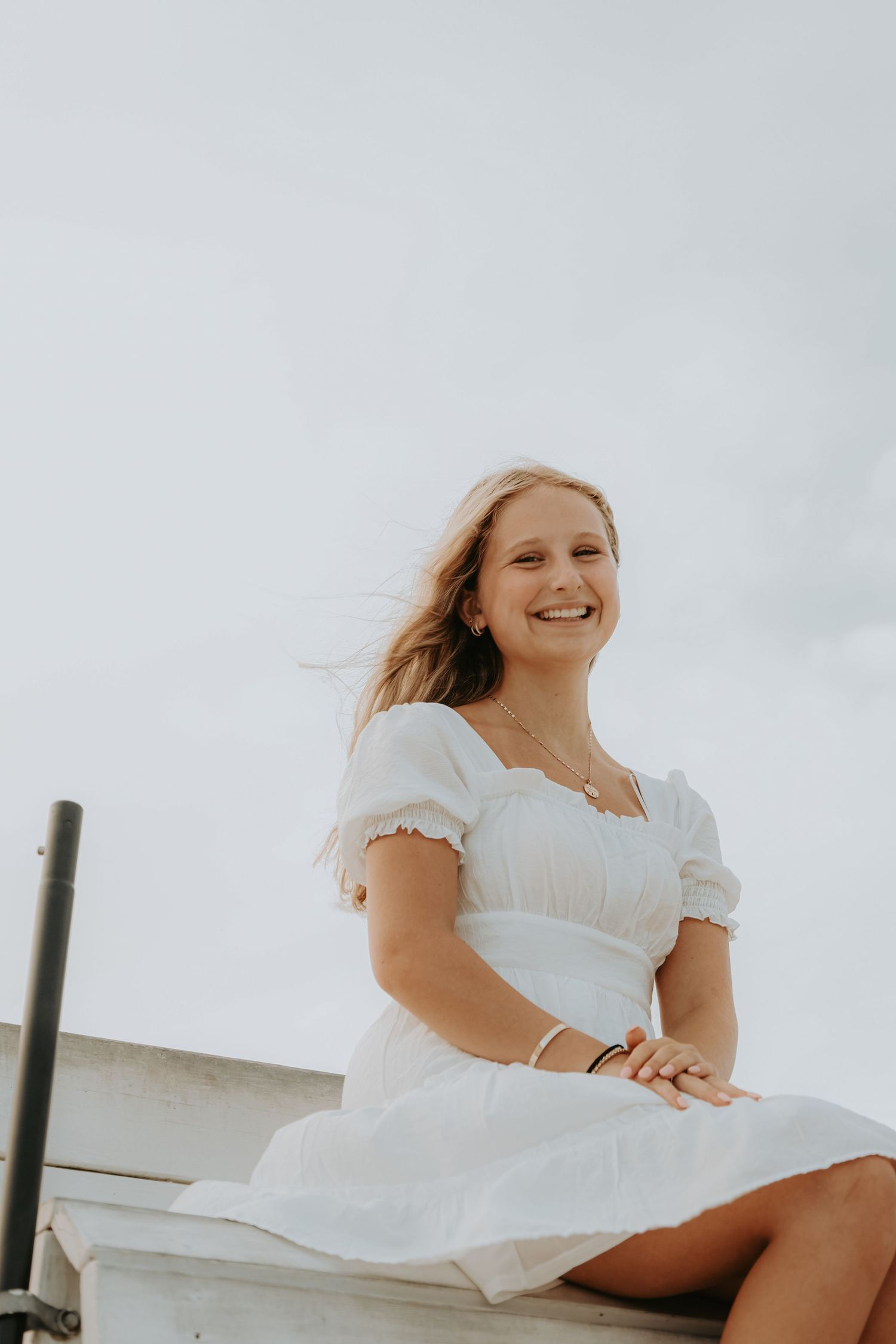 Woman in white dress sitting outdoors with wind blowing through her hair.