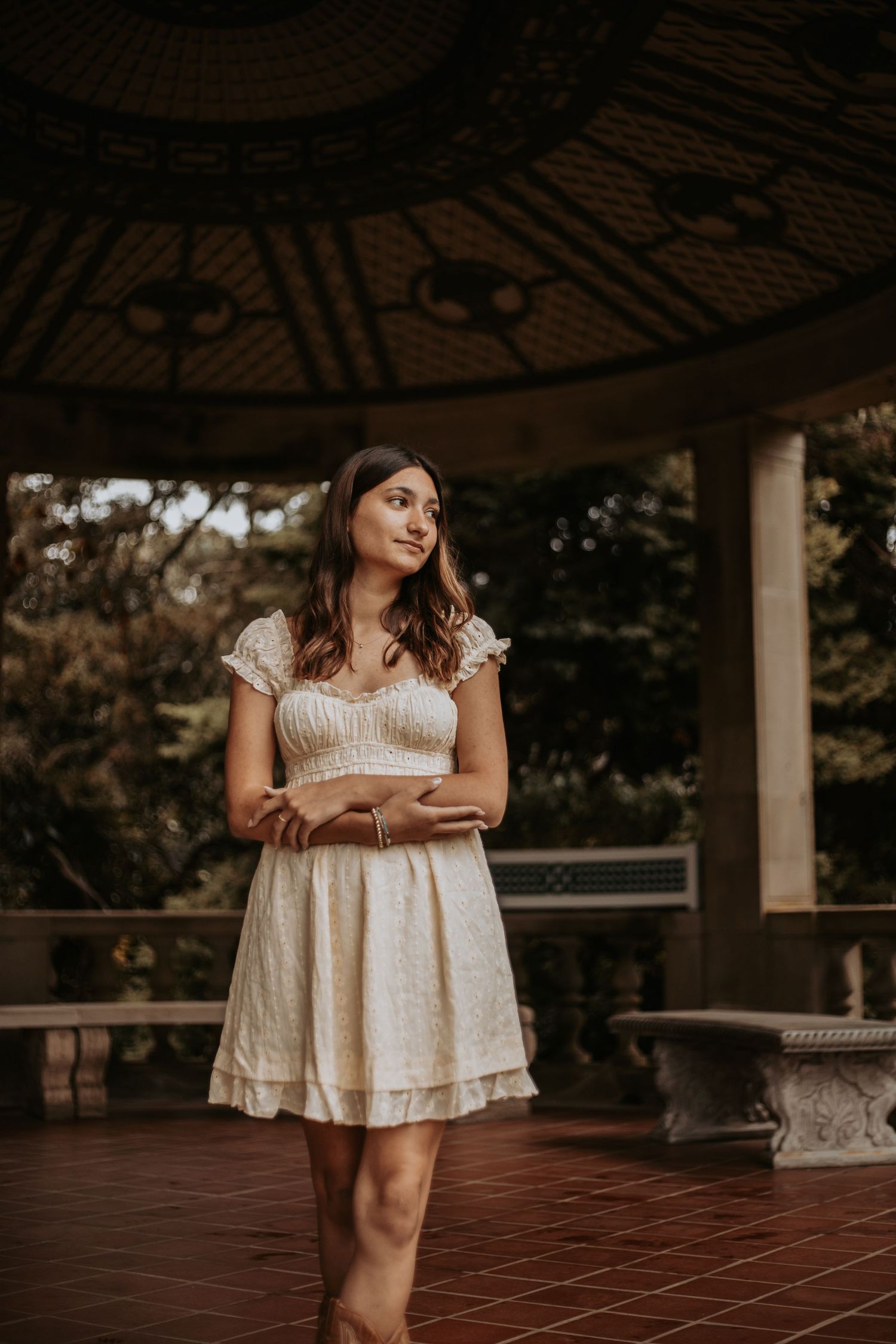 A person in a cream-colored dress poses in sections against a rustic gazebo backdrop with terracotta flooring.