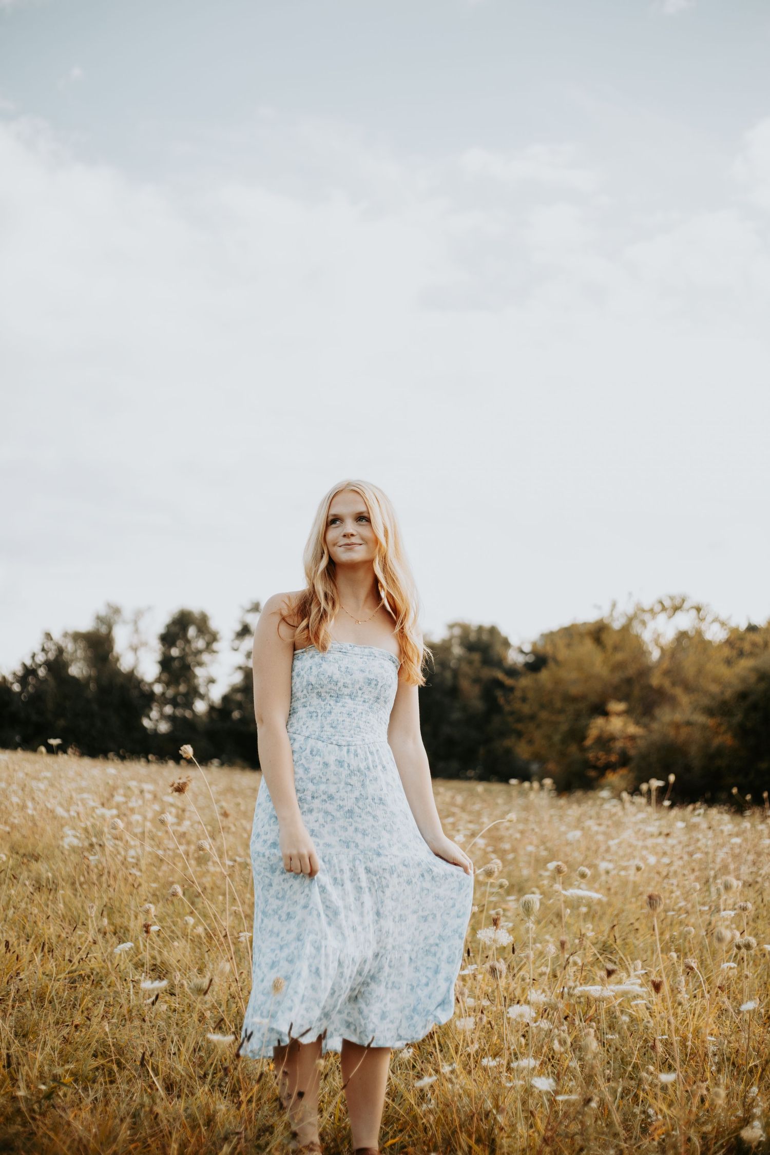 A person in a floral sundress twirls playfully in a golden sunlit meadow during summer.