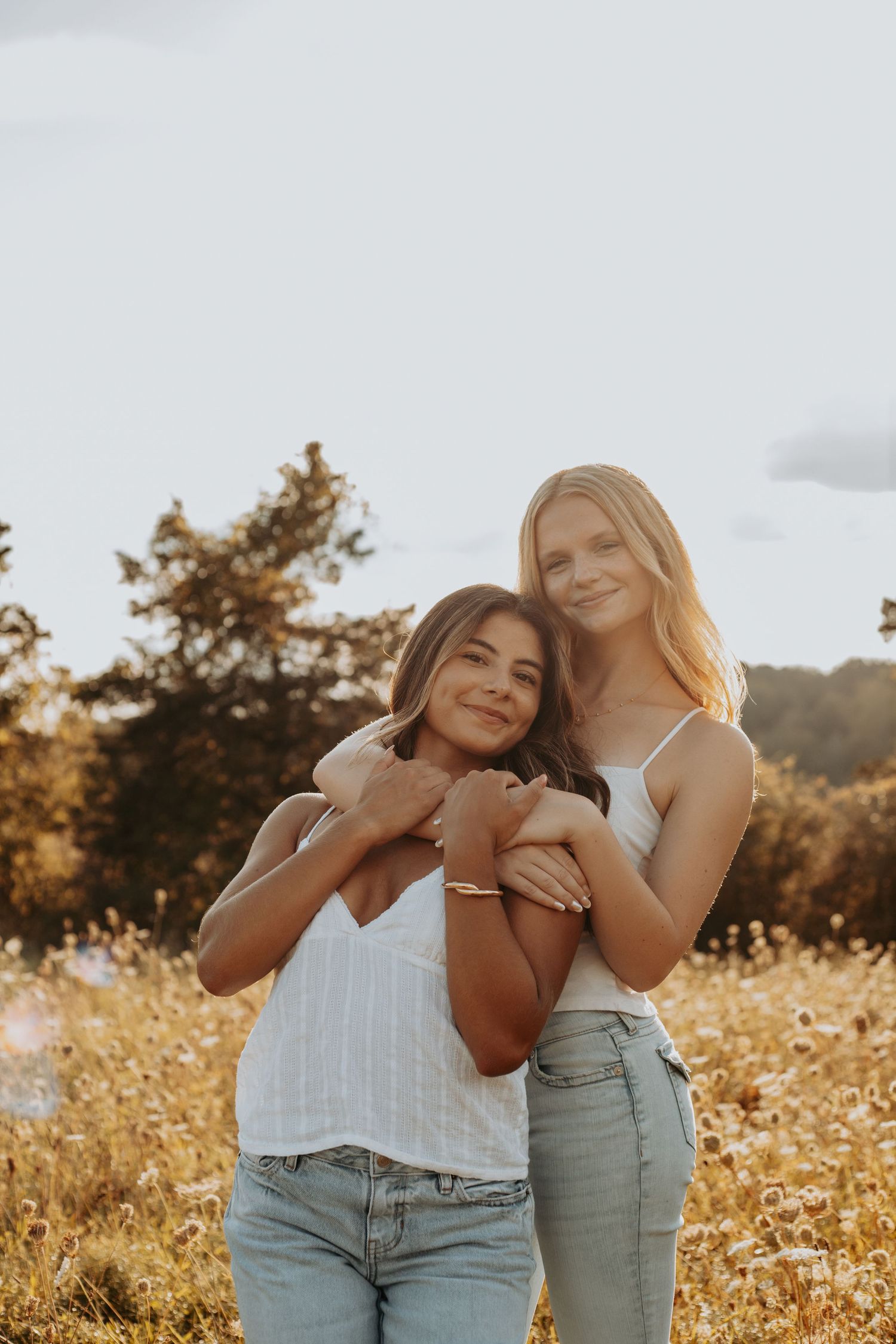 Two friends share joyful moments together in a golden field at sunset.
