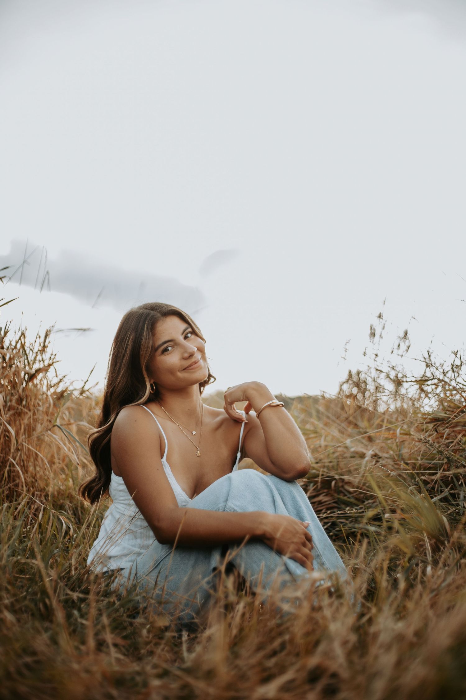 A person sits thoughtfully in a field of dried golden grass during sunset with soft lighting and a dreamy atmosphere.