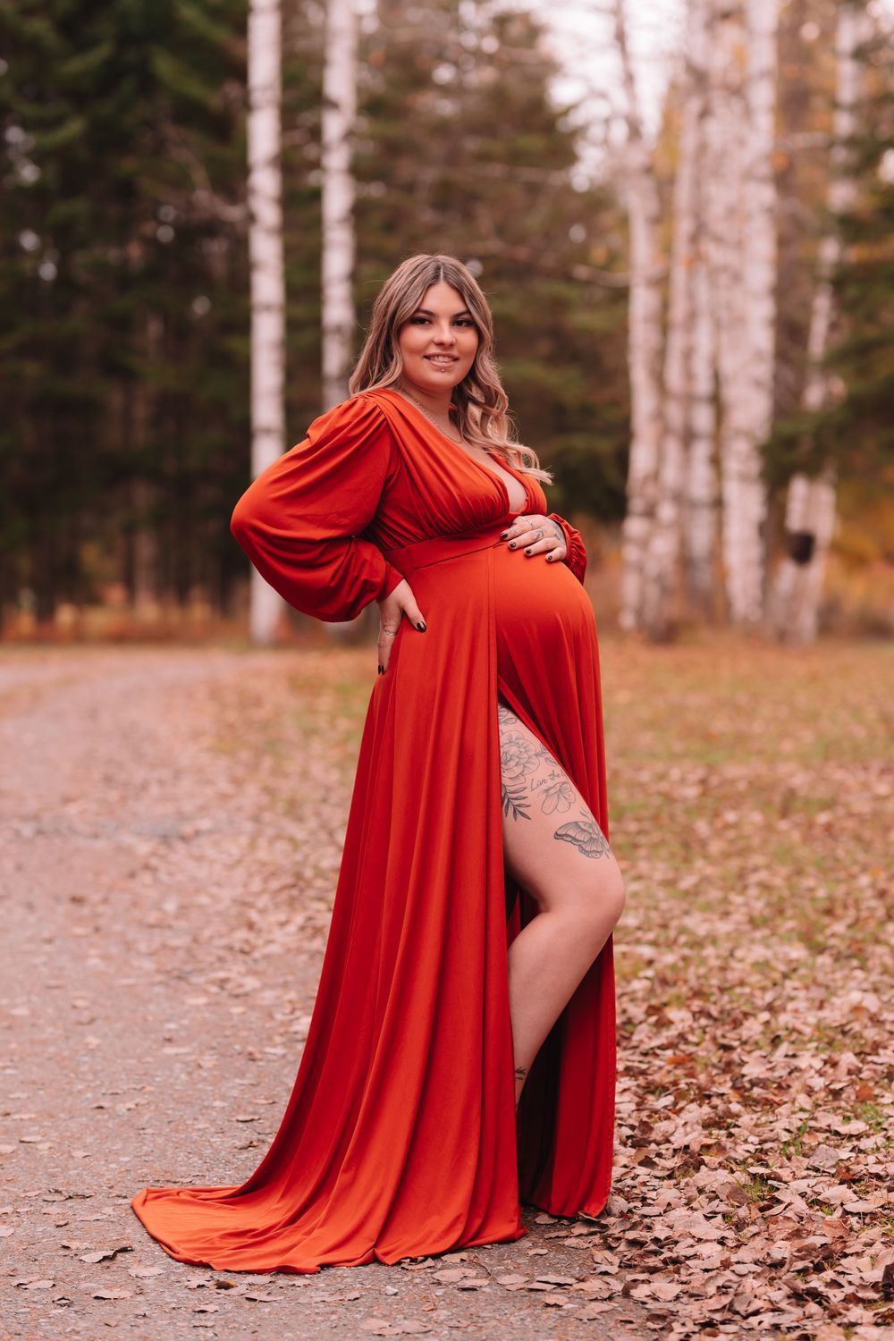 Maternity portrait featuring flowing red dress on autumn forest path.